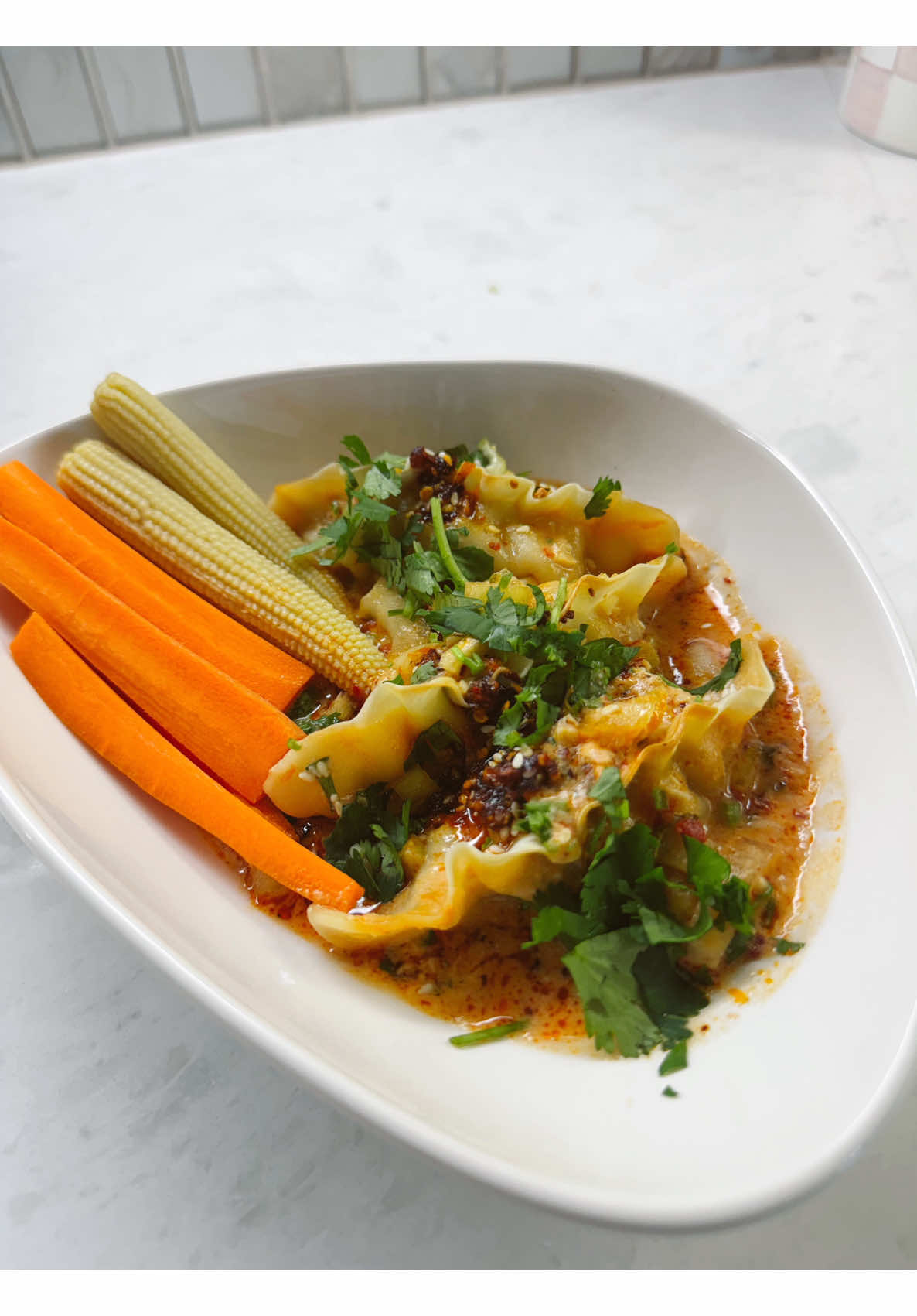 Making spicy chili oil dumplings topped with cilantro, baby corn, and sweet carrots