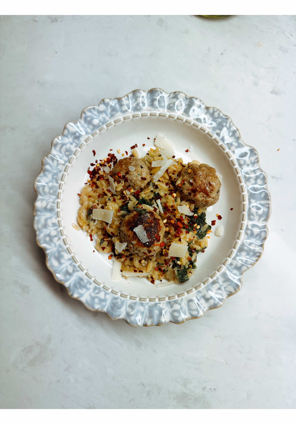 Making homemade italian meatballs over orzo with spinach, parmesan, and red pepper